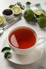 Cup of tasty bergamot tea and fresh fruits on white table