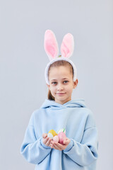 Vertical portrait of cute teenage girl wearing bunny ears and holding Easter eggs against white background, copy space