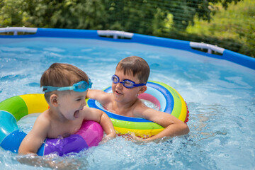 Two boys brothers in the outdoor outdoor pool near the house swim and play. Colored, swimming,...