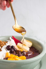 acai bowl with bananas, mango, blueberries, coconut, granola, serving honey.  marble background. © yennyleen
