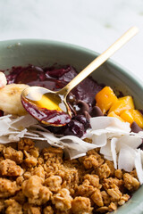 acai bowl with bananas, mango, blueberries, coconut, granola, honey.  marble background.