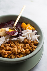 acai bowl with bananas, mango, blueberries, coconut, granola, honey.  marble background.