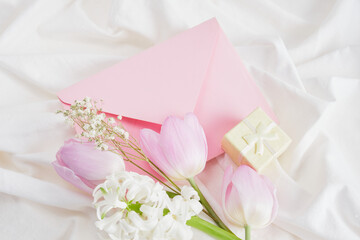 a bouquet of spring flowers in delicate shades, a small yellow gift box and a pink envelope on the bed