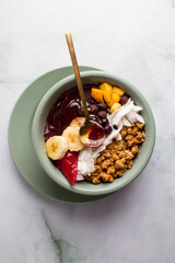 acai bowl with bananas, mango, blueberries, coconut, granola, honey. flat lay marble background.