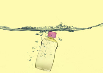 Bottle of baby oil in water against yellow background