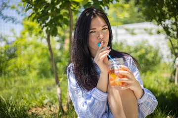 Portrait of happy young brunette woman posing drinking fresh fruit cocktail relaxing at summer park