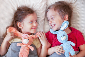 brother and sister are lying in bed with knitted bunnies and laughing