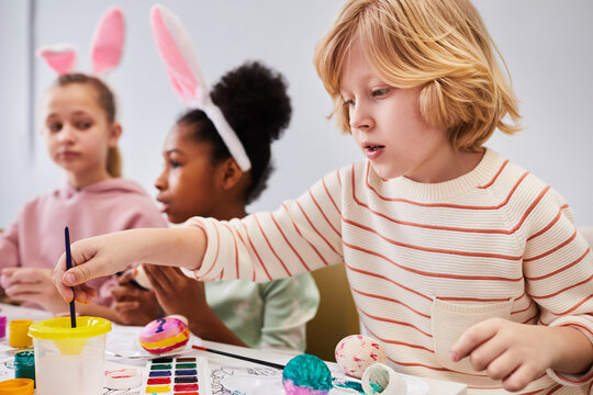 Group of children painting Easter eggs and wearing bunny ears while enjoying art and craft class in school