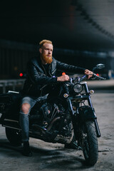 Portrait of young biker. Bearded red-haired man sits astride motorbike.