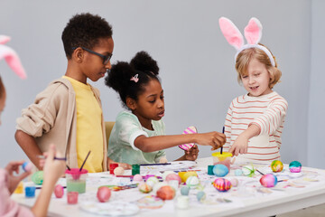 Minimal portrait of diverse group of children painting Easter eggs together while enjoying art and craft class
