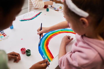 High angle shot of little girl drawing rainbow in bright colors while enjoying art and craft class,...