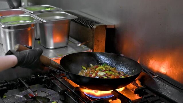 Slow motion of Chef Cookin wokg in the Kitchen. Restaurant wok fire cooking Close up, cook frying vegetable in the commercial kitchen. High quality FullHD footage