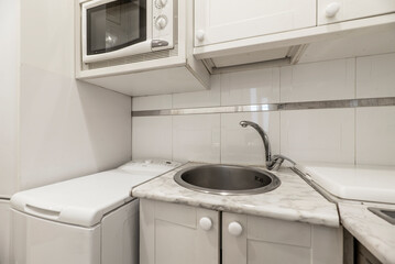 Small white kitchen with marble-like wood countertops with appliances, stainless steel sink, microwave and dishwasher