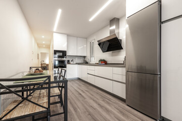 glass dining table next to fitted kitchen with appliance and fridge in foreground