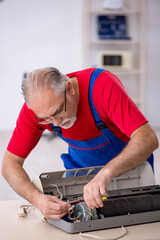 Old repairman repairing air-conditioner at workshop