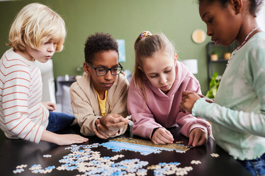Portrait of diverse group of children playing with puzzle game indoors together