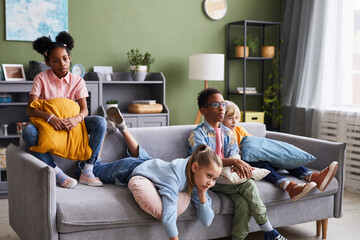 Diverse group of children watching TV at home while lounging on sofa looking bored