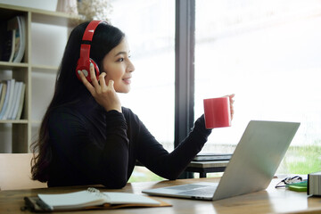 Tranquil young asian woman freelancer wearing headphone and drinking hot beverage at her workplace.