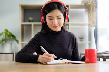 Pretty asian woman listening to music with wireless headphone and writing her diary.