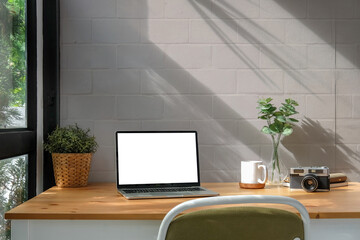 Laptop computer, coffee cup, potted plan and camera on wooden table.