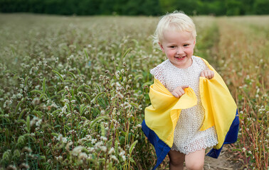 flag of Ukraine in the hands of a Ukrainian girl. A happy smiling child in a field runs along a rural road. Day of Defenders and Defenders of Ukraine
