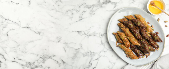 Delicious baklava with pistachio nuts and honey on white marble table, flat lay. Space for text