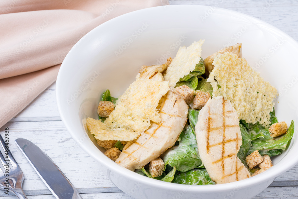 Wall mural Salad caesar with chicken on white plate on white wooden table macro close up