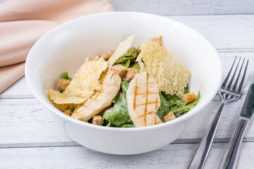 Salad caesar with chicken on white plate on white wooden table