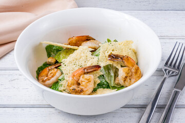 salad caesar with shrimps on white plate on white wooden table