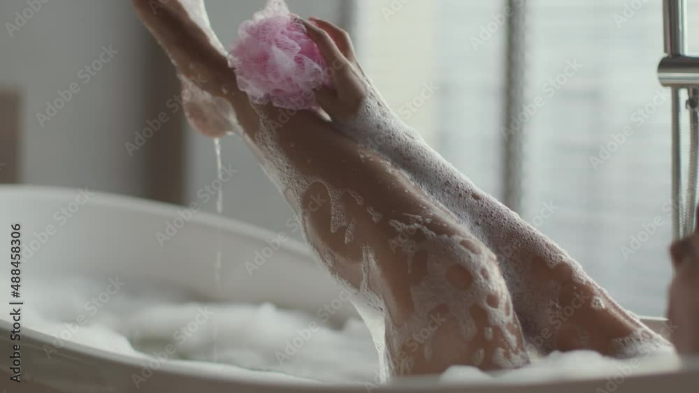 Wall mural Relax and hygiene concept. Young african american woman taking foamy bath, washing her leg with sponge, free space