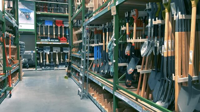 Hardware store departments and shelves with rows of shovels and hand carts for gardening or construction