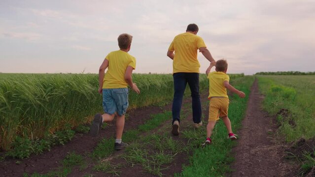 Happy family, children dad run together along the road in the field. The family team is playing outdoors. Kid father son teamwork. The concept of success and victory, the boy runs. Childrens team