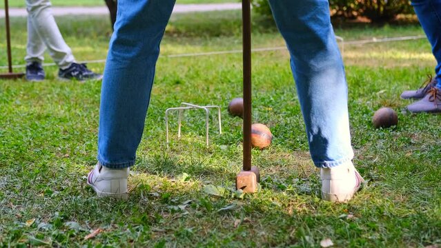 Person plays a sports game of croquet on a green field strike mallets on a ball and conducts through hoops. 