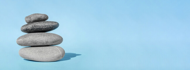 Obraz na płótnie Canvas Balanced pebble stones for spa treatments on blue background. The balancing cairn - symbol of harmony, tranquility and relaxation, concept of meditation. Stack of spa hot stones. Banner, copy space