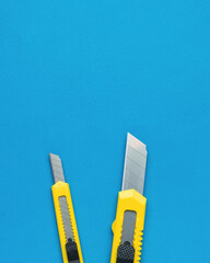 Two bright yellow stationery knives on a blue background. Flat lay. - obrazy, fototapety, plakaty