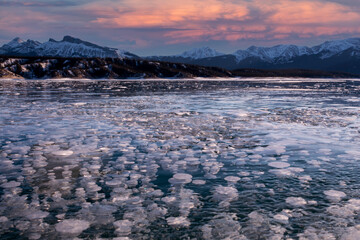 Sunset on Abraham lake in winter when the ice has trapped thousands of methane gas bubbles beneath the ice. Mountains in distance