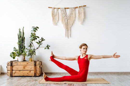 Yoga instructor in a red suit. girl builds the Pose of Ananthasana. Development of stretching and flexibility of the body. Time to calm down and be alone with yourself
