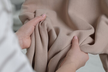 Woman touching clothes made of soft beige fabric indoors, closeup