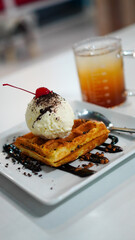 Close up photo of chocolate Waffle topped with ice cream and cherries.