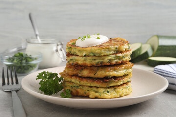 Delicious zucchini fritters with sour cream on grey table