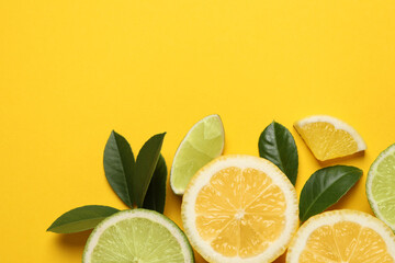 Fresh ripe lemons, limes and green leaves on yellow background, flat lay. Space for text