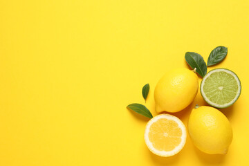 Fresh ripe lemons, lime and green leaves on yellow background, flat lay. Space for text