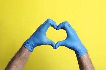 Doctor in medical gloves making heart with hands on yellow background, closeup