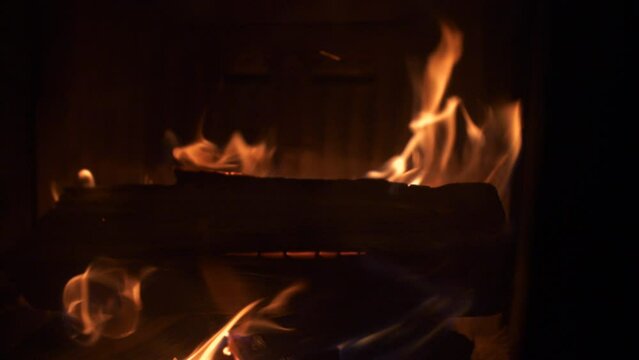 Burning firewood in home fireplace with flying sparkles around, close up shot