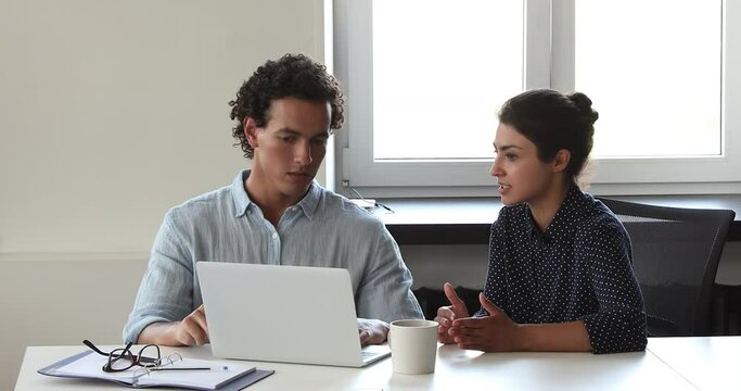 Diverse colleagues discuss online project seated at workplace desk, use laptop consider collaborative on-line task, working together in office. Teamwork, workflow, modern tech, new software concept