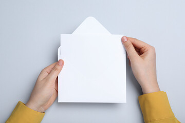 Woman taking card out of envelope on light grey background, top view