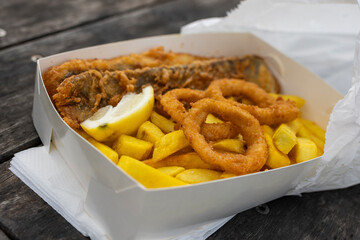 Takeaway fish and chips with battered calamari rings on a park table with copy space
