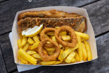 Takeaway fish and chips with battered calamari rings on a park table with copy space