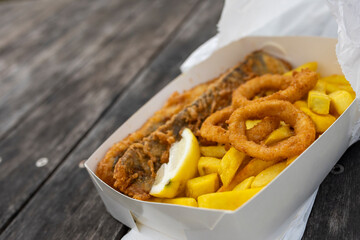 Takeaway fish and chips with battered calamari rings on a park table with copy space
