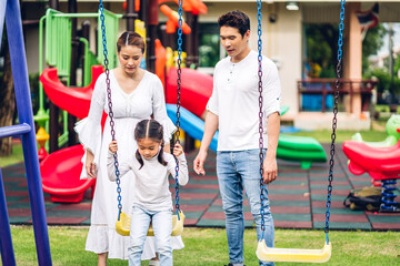 Fototapeta na wymiar Portrait of enjoy happy love asian family father and mother with little asian girl smiling playing and pushing daughter on the swing moments good time at playground